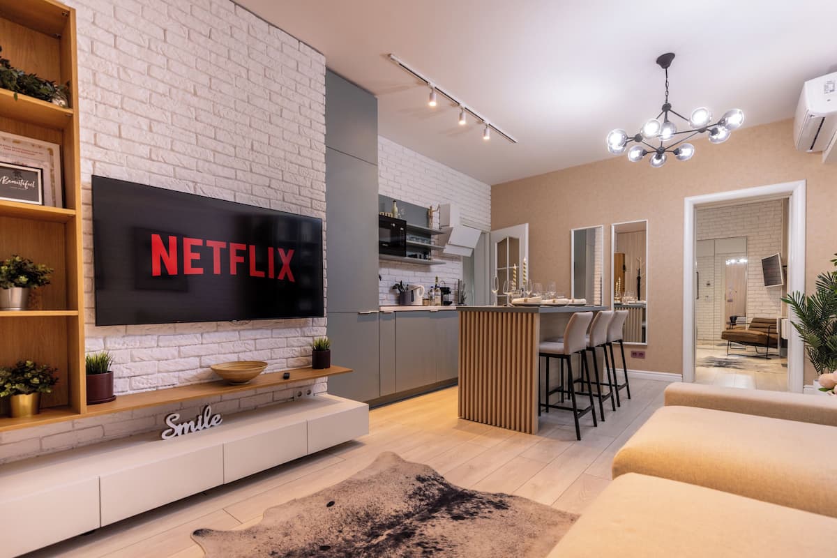 Un salon moderne doté d’un téléviseur à écran plat affichant le logo « NETFLIX », d’un coin cuisine et d’un espace repas.