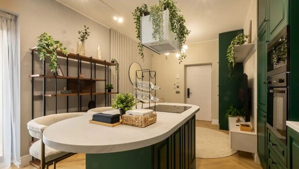 Une cuisine moderne avec un îlot central, des meubles de couleur verte et des plantes suspendues.