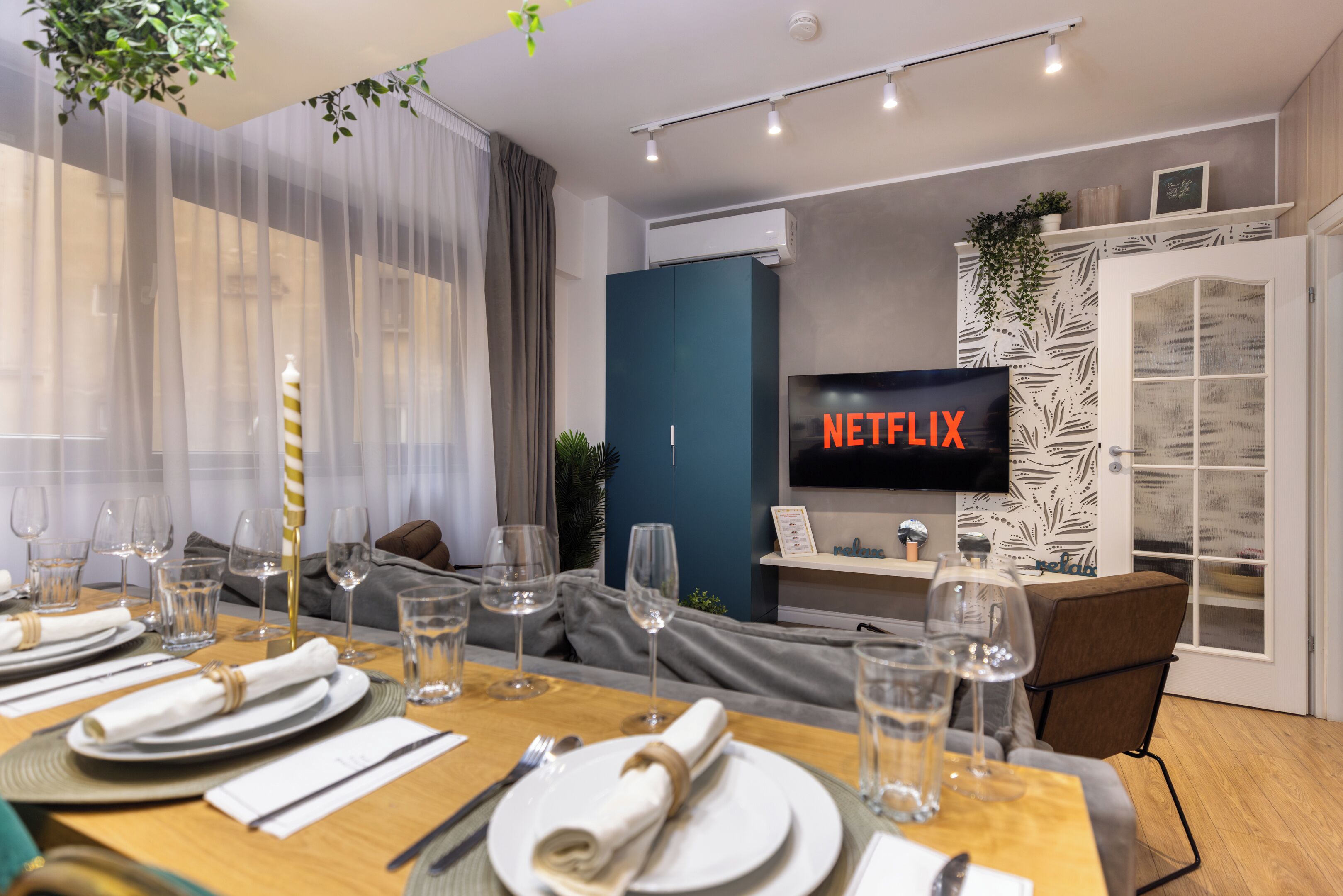 Ein modernes Wohnzimmer mit Essbereich, gedecktem Tisch und einer gemütlichen Sitzecke. Ein Fernseher zeigt 'NETFLIX'.