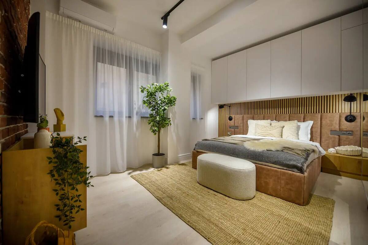 Une chambre moderne avec un grand lit, une plante en pot et une tête de lit en bois.