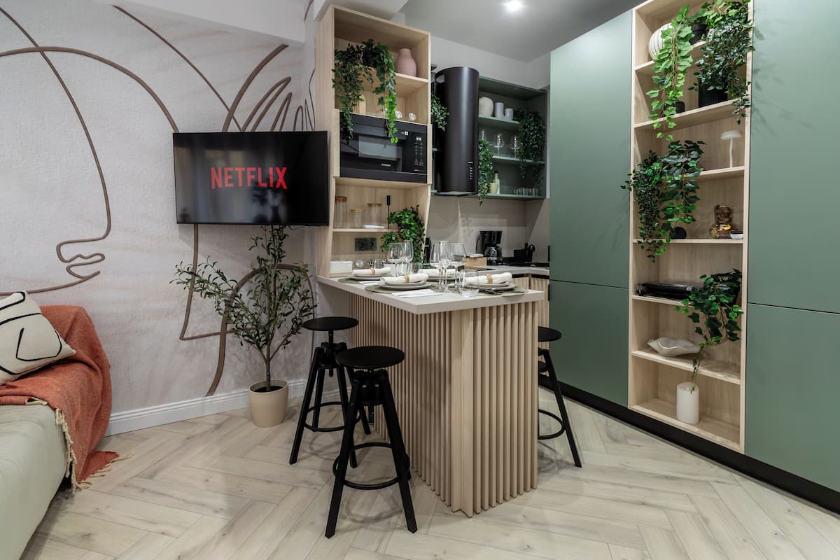 Une cuisine moderne dotée d’un îlot central, de tabourets de bar et d’un téléviseur diffusant du contenu « NETFLIX ».