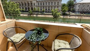 Un balcon avec deux fauteuils en osier et une petite table, d’où l’on peut admirer une rivière et des bâtiments historiques.
