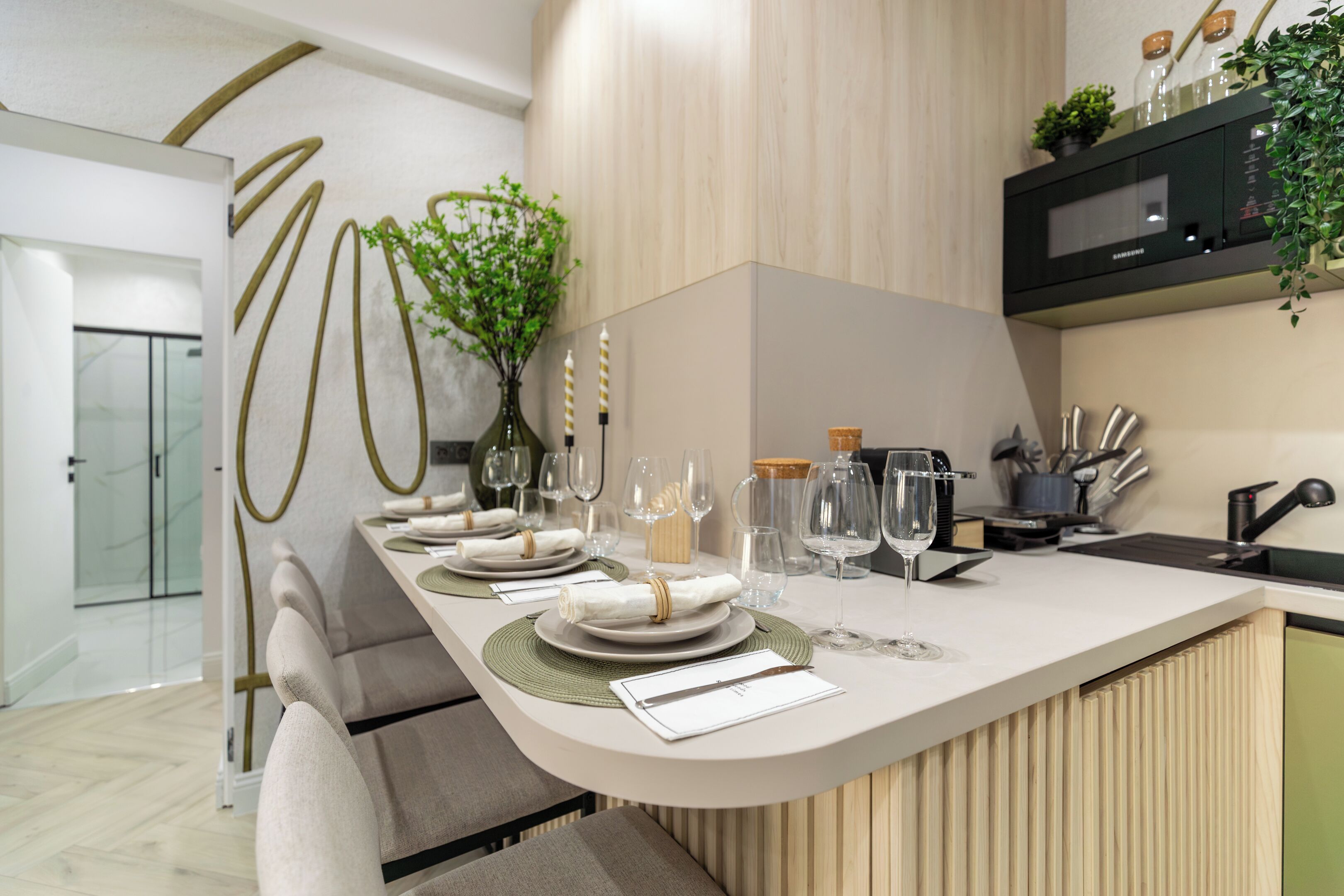 Una cocina moderna con cubierta blanca, microondas y fregadero. Hay copas de vino y un florero con flores sobre la cubierta.