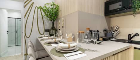 A modern kitchen with a white countertop, a microwave, and a sink. There are wine glasses and a vase with flowers on the counter.