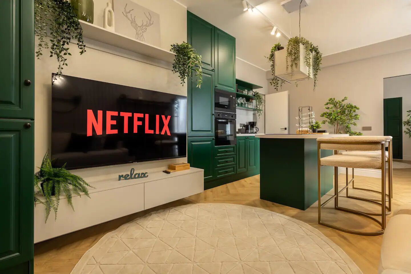 A modern kitchen with green cabinetry, a large flat-screen TV, and a bar area with a stool.