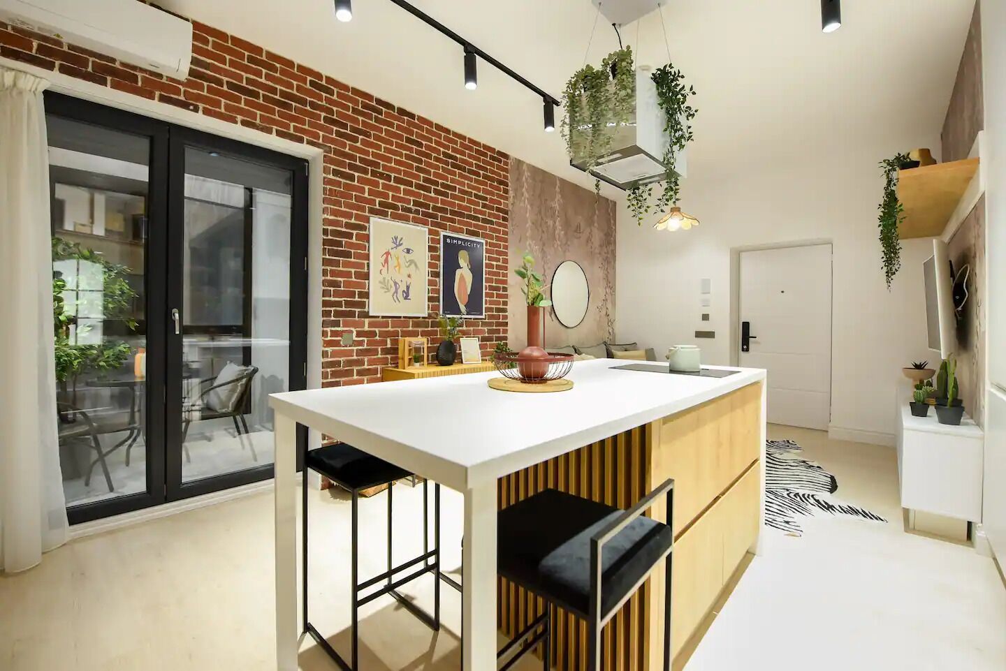 A modern kitchen with a central island, a brick wall, and hanging plants.