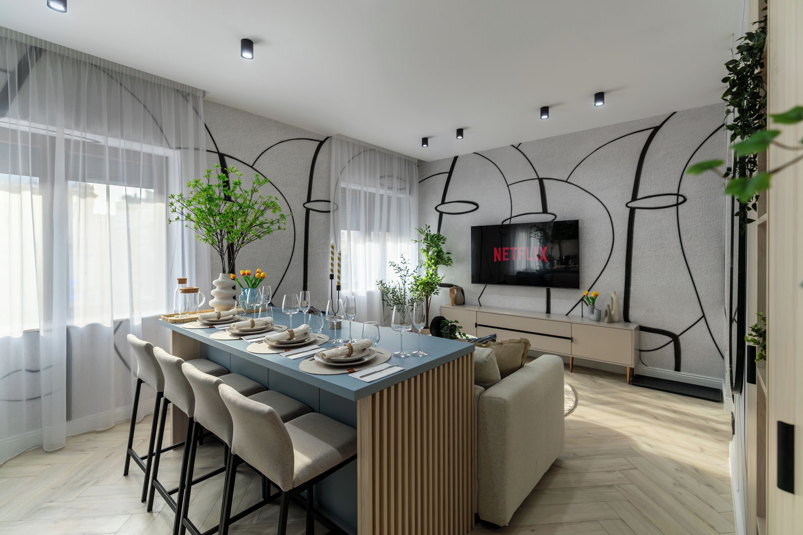 A modern dining area with a long table, bar stools, and a TV mounted on the wall.