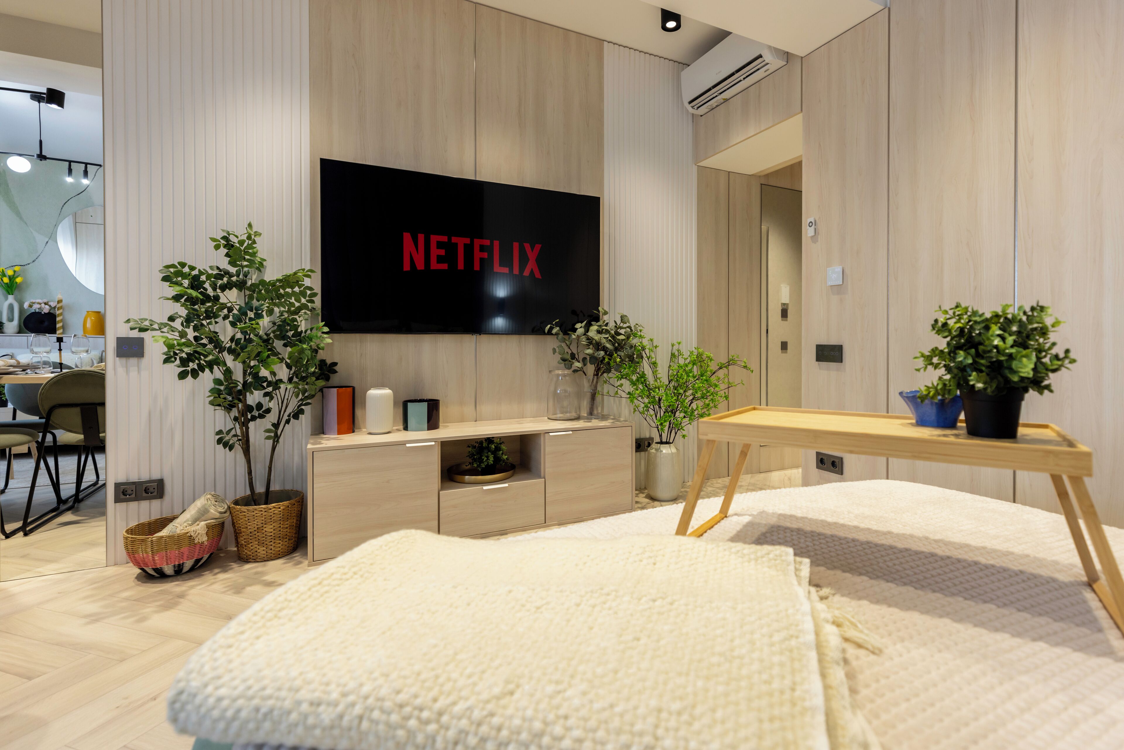 A modern living room with a flat-screen TV, wooden furniture, and two potted plants.