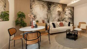 Una sala de estar moderna con una mesa redonda de comedor, dos sillas, un sofá con cojines decorativos, una mesa de centro y un mural grande en la pared.