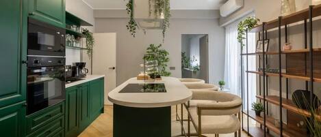 A modern kitchen with green cabinets, a central island, and hanging plants.