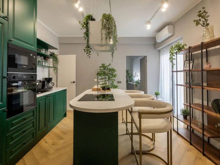A modern kitchen with green cabinets, a central island, and hanging plants.