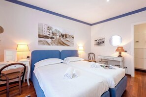 Ein Hotelzimmer mit zwei Betten, einem Schreibtisch, einem Stuhl und einer Wandlampe.
