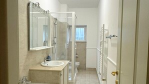 Un baño estrecho y bien iluminado con bañera, lavamanos y zona de ducha.