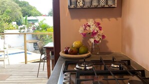 Une cuisine avec une cuisinière à gaz, un saladier rempli de fruits et un vase de fleurs. Une étagère se trouve au-dessus de la cuisinière, où sont disposés des objets décoratifs.