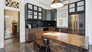 A modern kitchen with dark cabinetry, a stainless steel refrigerator, and a wooden dining table with wire chairs. - Paton House, Beach 250m | Heritage Luxe w/ Fireplace and 86" TV (South Fremantle)