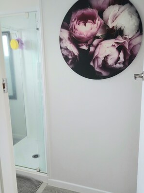 A bathroom with a glass shower door, a white sink, and a wall-mounted circular artwork of flowers.