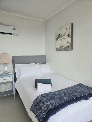 Una cama bien tendida con sábanas blancas, cabecera gris y una manta con estampado azul y blanco.
