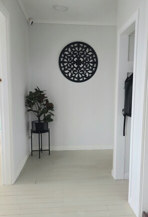 Un pasillo con piso blanco, un elemento decorativo negro en la pared y una planta en maceta.