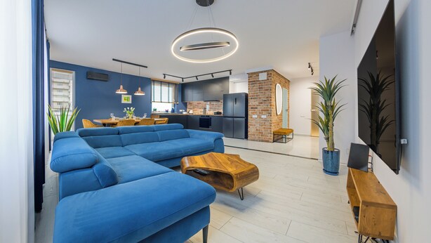 Una sala de estar moderna con un sofá seccional azul, una mesa de centro de madera y una cocina al fondo.