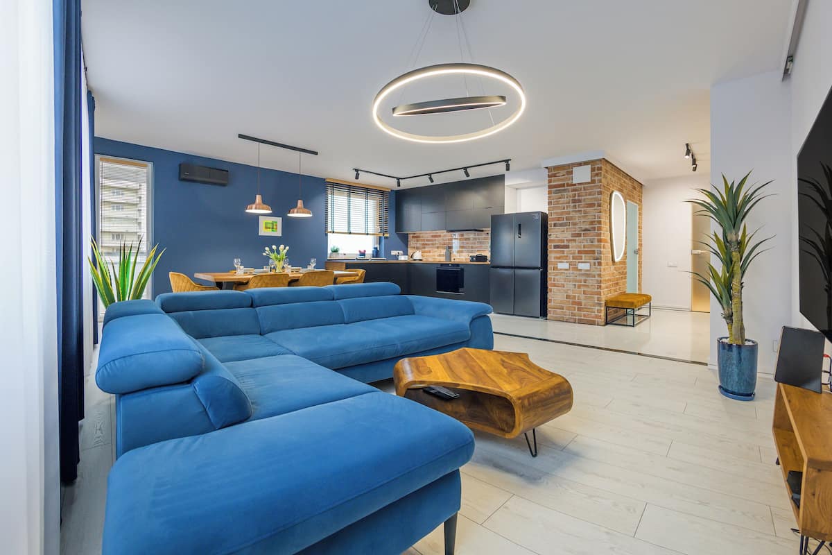 A modern living room with a blue sectional sofa, a wooden coffee table, and a kitchen in the background.