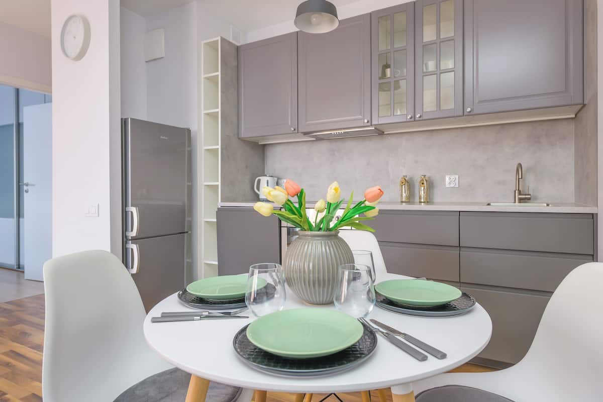 A modern kitchen with grey cabinets, a stainless steel refrigerator, and a dining area with a round table set for four.
