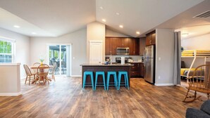 A spacious kitchen with wooden cabinets, a central island with stools, and a dining area with a table and chairs. - Boutique CDA Retreat | Sleeps 6 • Near Downtown (Coeur d'Alene)