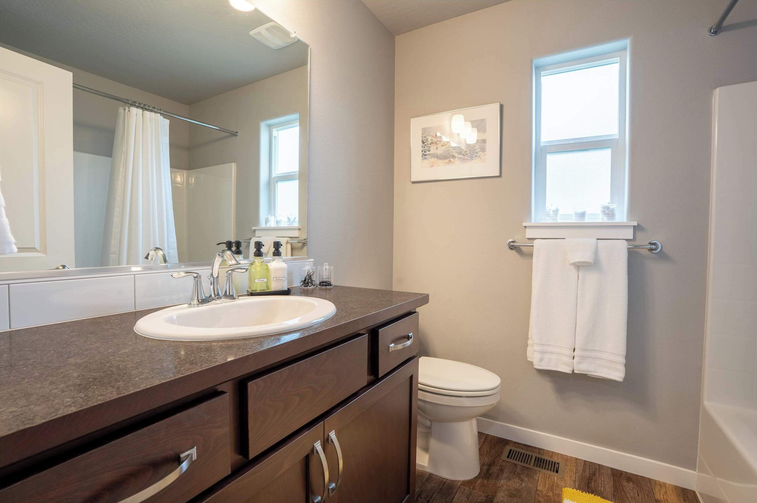 A bathroom with a sink, mirror, toilet, and a window.
