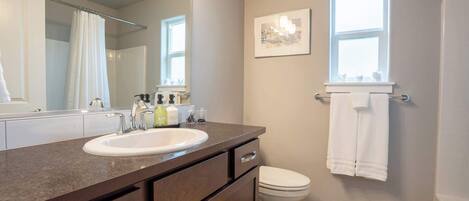 A bathroom with a sink, mirror, toilet, and a window.