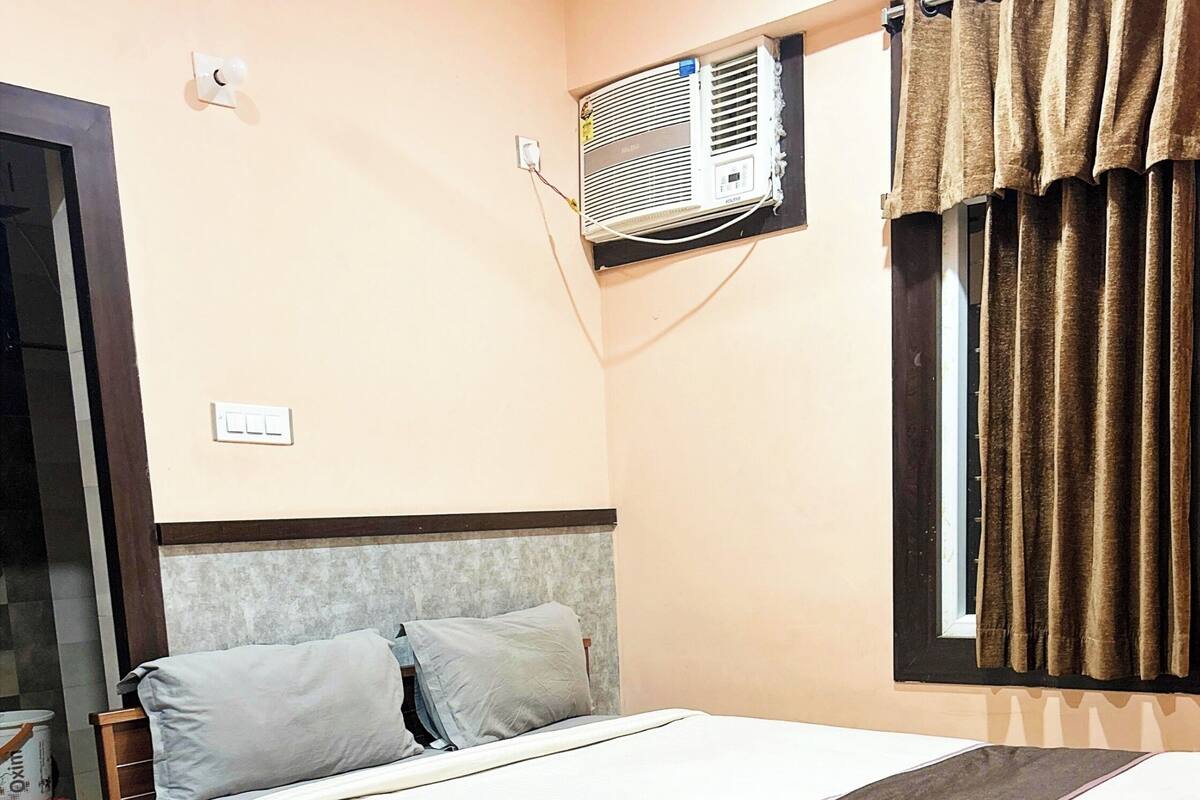 A bedroom with a wooden bed, a wall-mounted air conditioner, and a window with curtains.