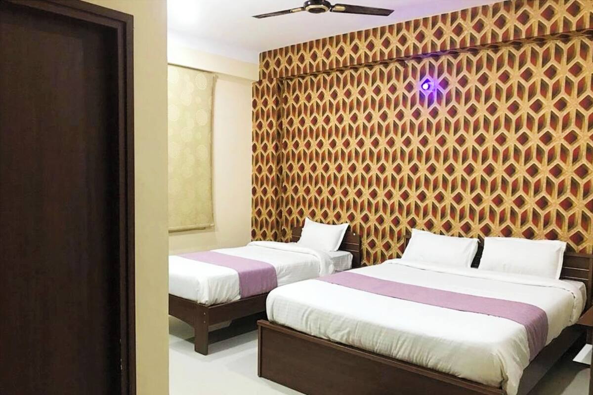 A hotel room with two single beds, a wooden headboard, a patterned wall, and a ceiling fan.