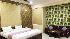 A hotel room with a bed, a sofa, and a wall with green plants.