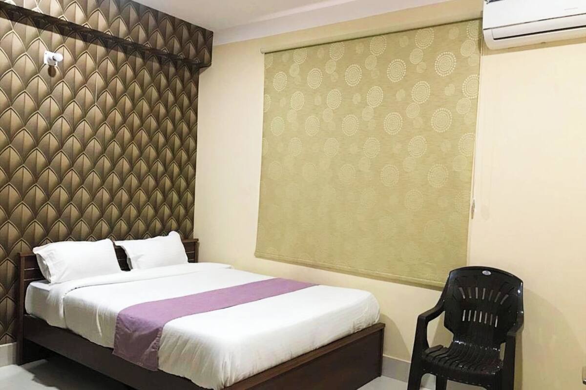 A hotel room with a bed, a chair, and a window with a patterned curtain.