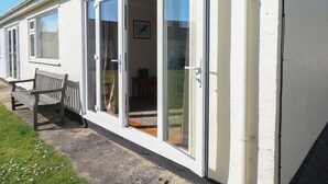 Une rangée de fenêtres à cadre blanc, dotées de portes-fenêtres coulissantes, un banc et une petite table.