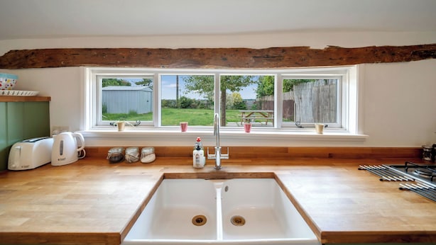 A kitchen with a large window, wooden beams, a sink, and various kitchen appliances. - Countryside Cottage in Bulmer- Sleeps 6/7 (Sudbury)