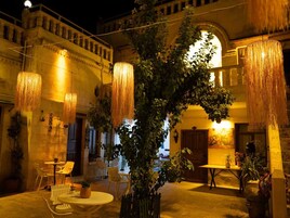 Un patio al aire libre con lámparas colgantes, mesas, sillas y plantas en macetas.