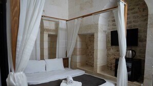 Una cama con dosel con sábanas blancas, un colchón oscuro y una toalla blanca sobre la cama.