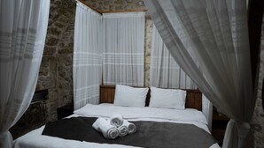 Una cama con sábanas blancas y una manta negra, un cabecero de madera y cortinas blancas.