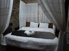 Una cama con sábanas blancas y una manta negra, un cabecero de madera y cortinas blancas.