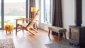 A cozy room with a wooden floor, a rocking chair, a bench, a small table, and a wood-burning stove.