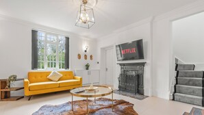 A living room with a yellow sofa, a round coffee table, a leather rug, a fireplace, and a staircase. - Charming,Spacious Manor House with Lake&Pool Table (Blakedown)