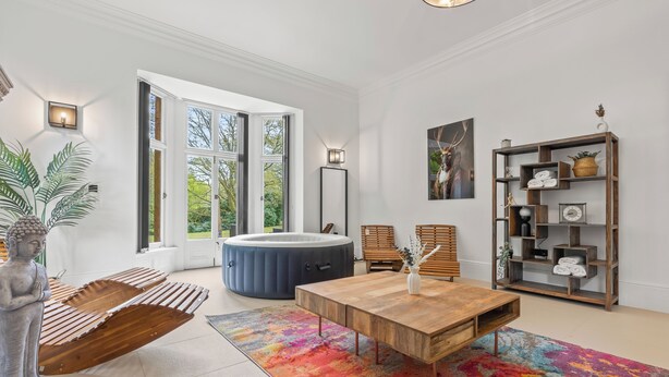 A spacious living room with a large window, a wooden coffee table, a colorful rug, and a wooden bookshelf. - Charming,Spacious Manor House with Lake&Pool Table (Blakedown)
