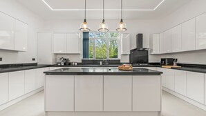 A modern kitchen with white cabinetry, a central island, pendant lighting, and a view through a window. - Charming,Spacious Manor House with Lake&Pool Table (Blakedown)
