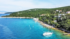 Eine Küstenlandschaft mit blauem Meer, einem vor der Küste verankerten weißen Boot und einer Reihung von Häusern entlang der Küste.