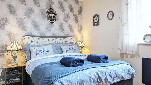 Un dormitorio con cama, dos lámparas de noche, una mesita de noche y una ventana con cortinas.