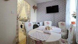 Un comedor con una mesa para dos, una lavadora y un televisor montado en la pared.