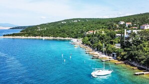 A coastal area with a clear blue sea, a white boat anchored near the shore, and a row of houses along the coastline.
