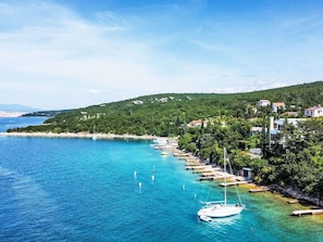 A coastal area with a clear blue sea, a small boat anchored near the shore, and a row of buildings along the coastline.
