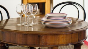 A round wooden dining table with four wine glasses and a stack of plates. - Accomodo MIB13 Bivano Navigli (Milan)
