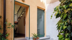 A courtyard with stone steps leading to a door, surrounded by greenery and a building with a visible staircase. - Accomodo MIB13 Bivano Navigli (Milan)