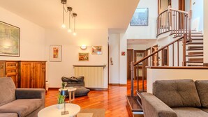 A spacious living room with a staircase leading to an upper level, wooden flooring, and a modern design.